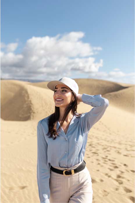 A young, attractive, and beautiful lady enjoys the dubai desert safari tour, standing on a sand dune with the expansive desert landscape stretching out behind her. She looks content and captivated by the serene beauty of the surroundings.