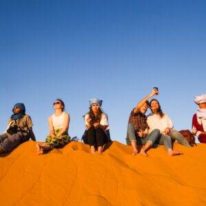 Group of People sitting on the top of dune and enjoy evening desert safari dubai tour