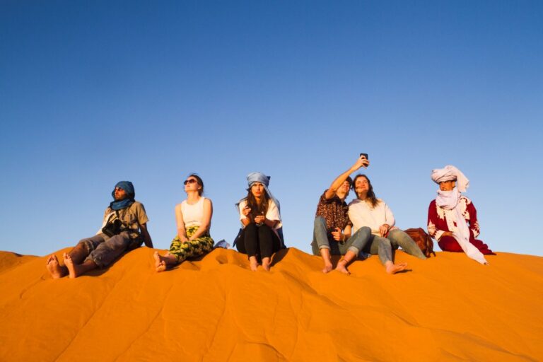 Group of People sitting on the top of dune and enjoy evening desert safari dubai tour